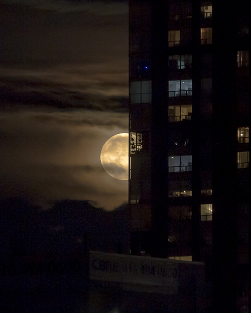 Moon partly peeking from behind an apartment building