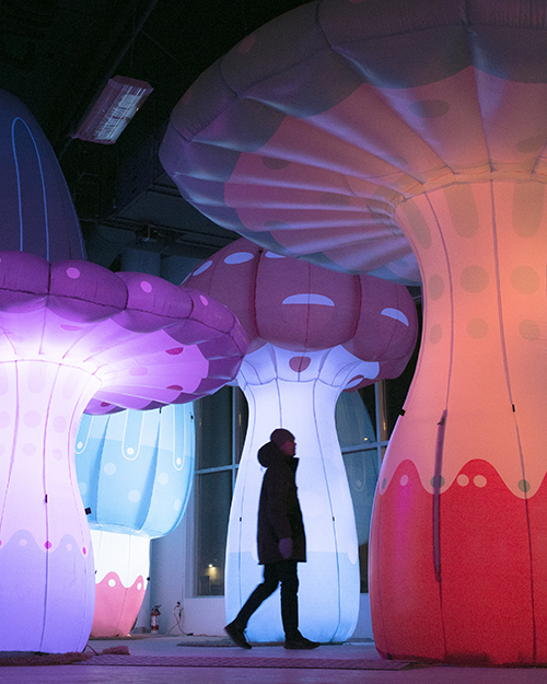 A man walking amongst lit up inflatable mushrooms