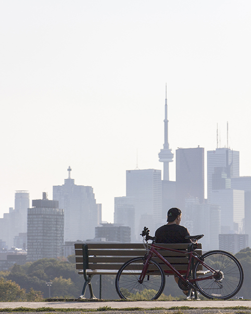 A man sitting on a bench with his bicycle and views of downtown Toronto