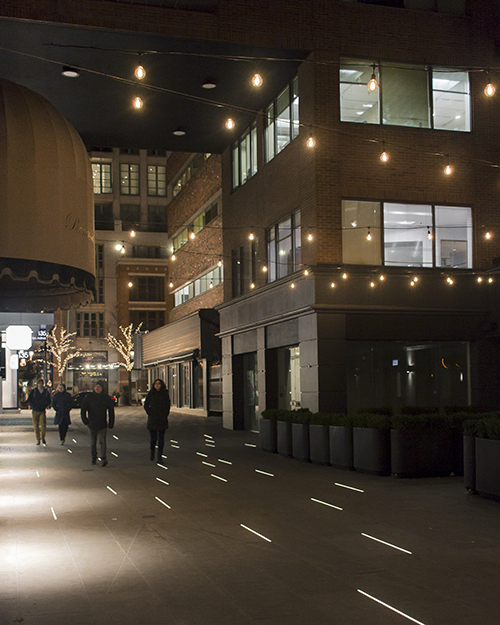A pedestrian walkway lit up with bulbs overhead and light strips on the ground